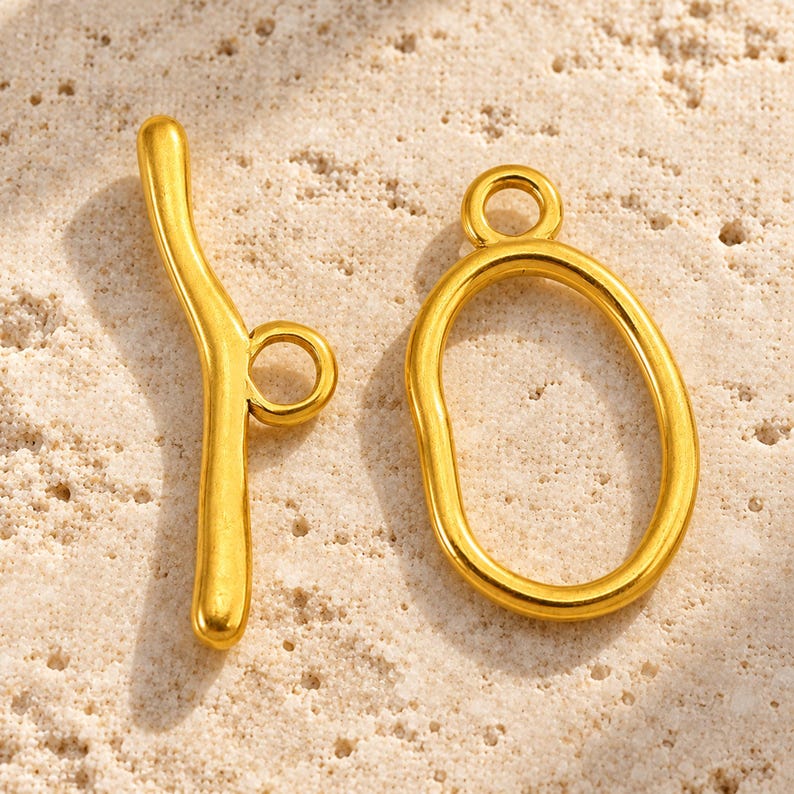 One Gold-G oval toggle clasp sample set with curved bar on pale natural stone.
