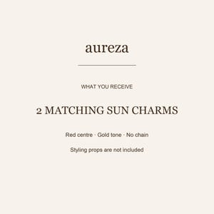 May include: A product information card with the text aureza, WHAT YOU RECEIVE, 2 MATCHING SUN CHARMS, Red centre, Gold tone, No chain, and Styling props are not included. The text is dark brown on a light cream background with a horizontal line.