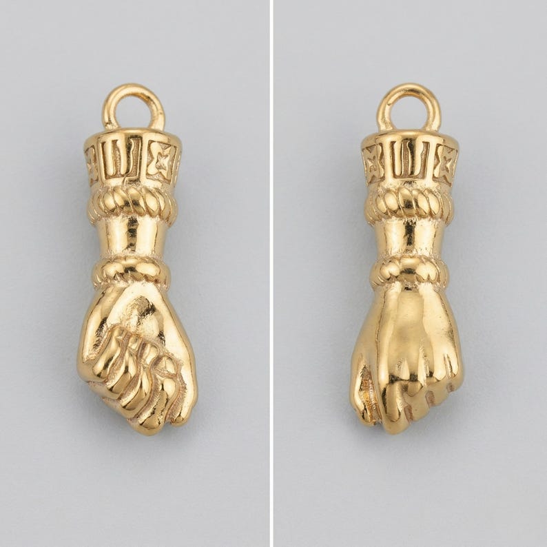 May include: A pair of gold-colored fist-shaped charms. Each charm features a detailed hand design with a loop at the top for hanging. The charms have a textured surface and are likely made of metal, suitable for jewelry making or decorative purposes.