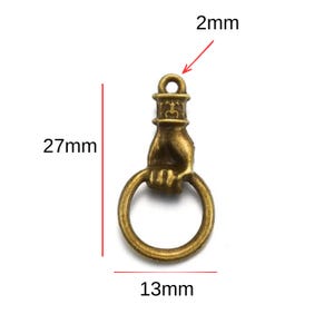 May include: Antique bronze-colored charm featuring a hand holding a ring. The charm measures 27mm in length, 13mm in width, and has a 2mm loop. This decorative charm is suitable for jewelry making and crafting projects.