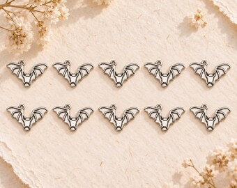 May include: Ten identical silver-toned metal bat charms arranged in two rows of five. Each charm features a stylized bat with outstretched wings and a small circular loop at the top for attachment, showcasing a detailed embossed design.