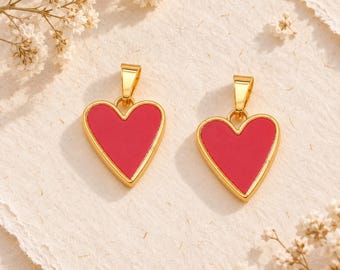 May include: Two heart-shaped pendants featuring a vibrant red enamel center encased in a polished gold-tone metal frame. Each pendant includes a small gold-tone bail at the top, designed for attachment to a necklace chain or other jewelry component.