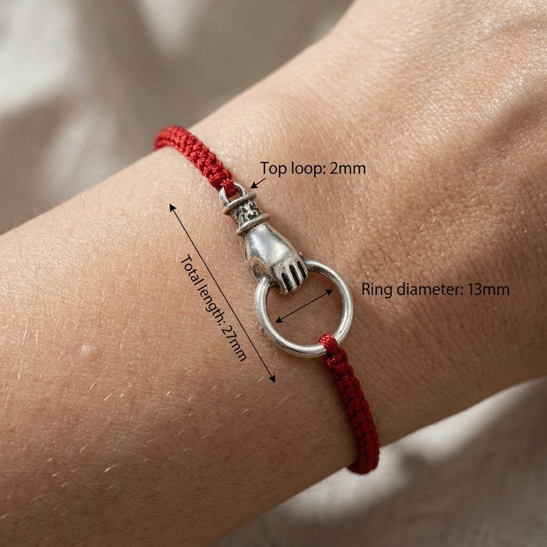 May include: Red cord bracelet featuring a silver hand clasping a silver ring. The total length is 2.7cm, the ring diameter is 1.3cm, and the top loop is 2mm.