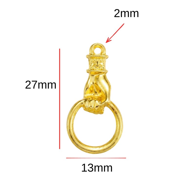 Puede incluir: Un dije dorado con forma de mano que sostiene un anillo. El dije mide 27 mm de largo, 13 mm de ancho y tiene un lazo de 2 mm. Probablemente est&aacute; hecho de metal y est&aacute; dise&ntilde;ado para la fabricaci&oacute;n de joyas o manualidades.