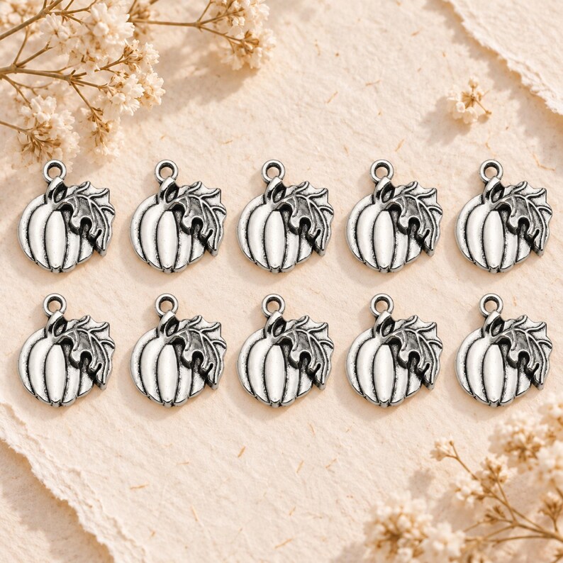 May include: A set of ten silver-toned metal charms, each shaped like a pumpkin with an attached leaf and a small circular loop at the top for hanging. The charms feature a detailed, embossed design with dark oxidized accents in the crevices.