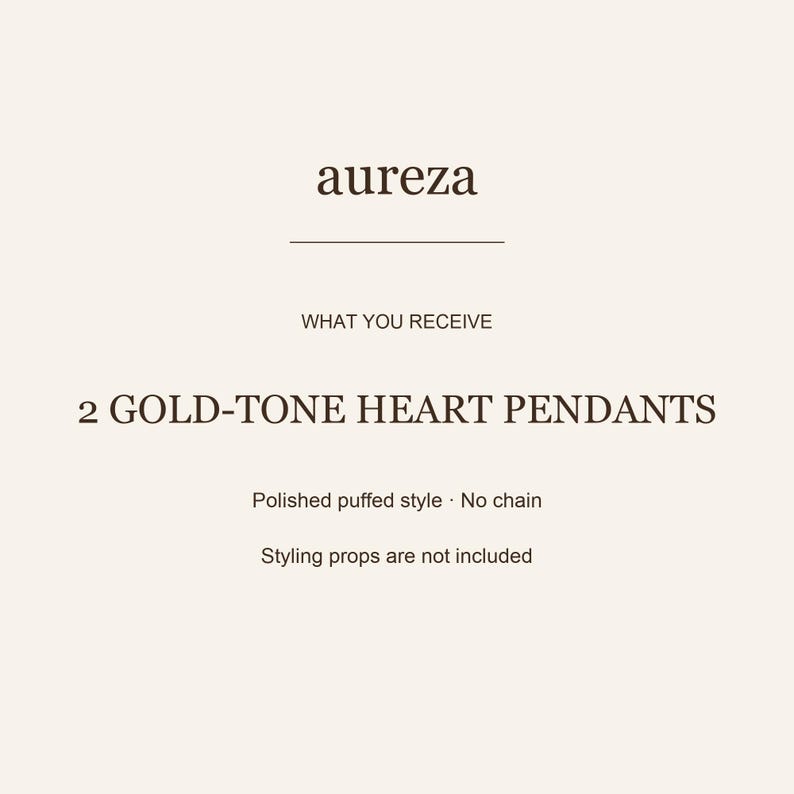May include: A product information card with the text aureza, WHAT YOU RECEIVE, 2 GOLD-TONE HEART PENDANTS, Polished puffed style, No chain, and Styling props are not included. The text is dark brown on a light cream background with a horizontal line.