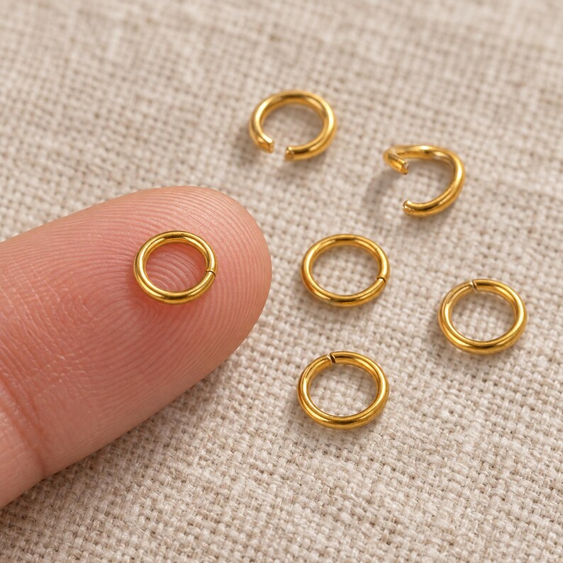 Gold-tone stainless steel open jump rings. Scale reference preview. 5mm diameter; 0.8mm wire. Buyer pack: 100 pieces.