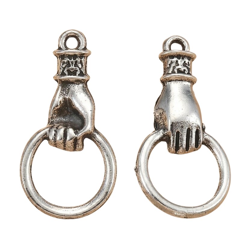 May include: Two silver-toned metal charms, each shaped like a hand grasping a circular ring. The hand features a cuff detail at the wrist and a loop at the top for attachment. The metal has a weathered, antiqued finish with dark recessed areas.