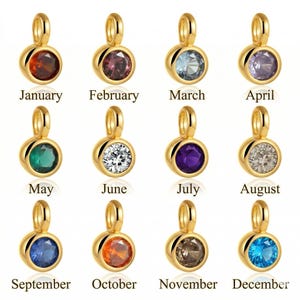 May include: Gold-colored pendants with birthstones for each month of the year. Each pendant features a round gemstone in a different color, with the month's name printed below. The gemstones include red, purple, blue, green, and clear.