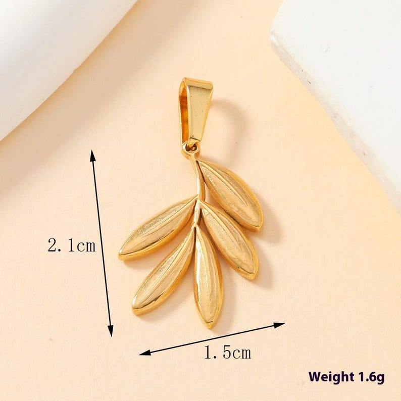 May include: A gold-colored metal pendant shaped like a small branch with five leaves. The pendant features a top bail for attachment. Dimensions are indicated as 2.1 cm in height and 1.5 cm in width, with a total weight of 1.6 grams.