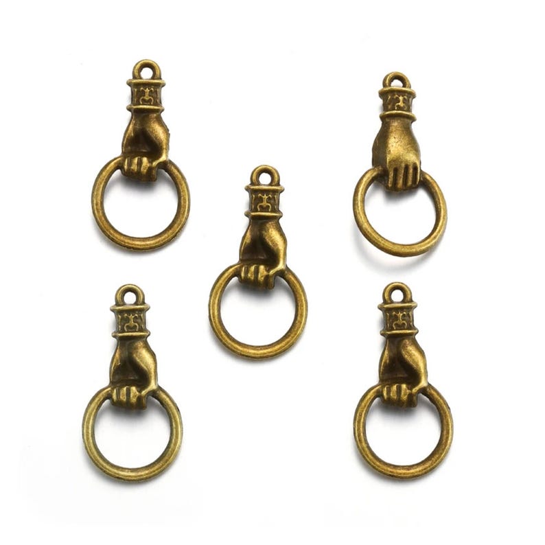 May include: Five antique bronze-colored charms. Each charm features a hand holding a ring, with a decorative top. The charms are arranged on a white background.