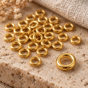 Gold-tone stainless steel closed jump rings. Macro detail. 4mm outer diameter; 1.2mm wire. Buyer pack: 50 pieces.