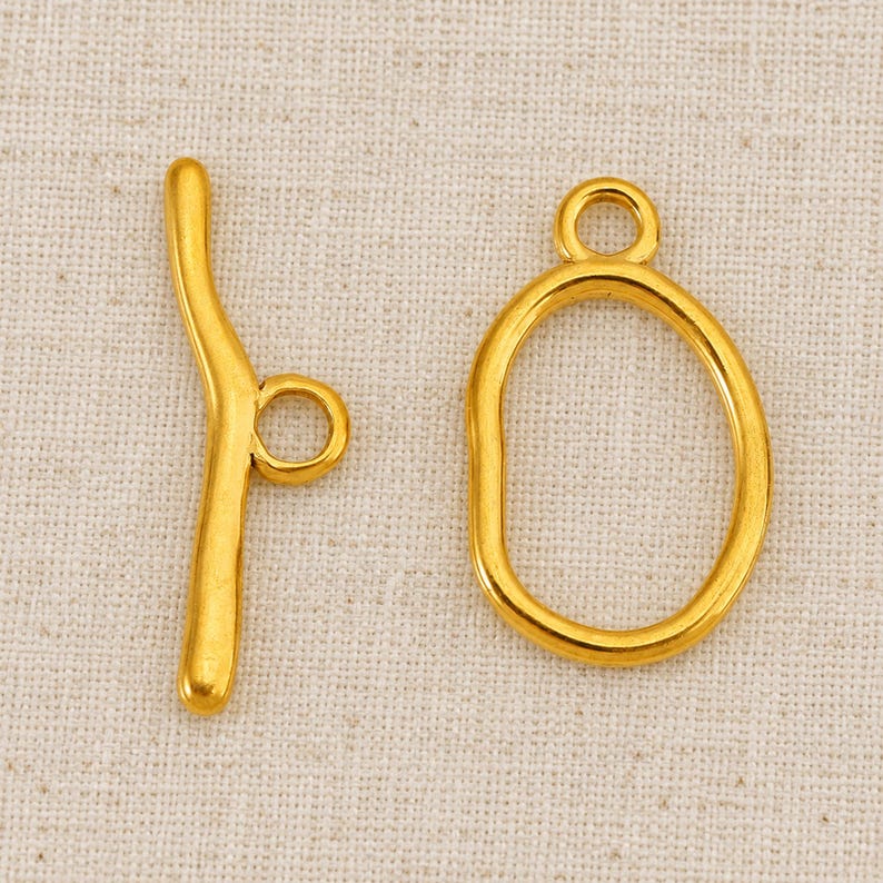 Gold-tone oval ring and curved T-bar toggle clasp, one Gold-G sample set on natural linen.