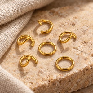 Gold-tone stainless steel open jump rings. Textured hero view. 5mm diameter; 0.8mm wire. Buyer pack: 100 pieces.