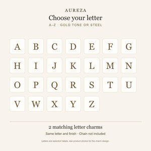 May include: A selection chart for letter charms featuring the brand name AUREZA, the text Choose your letter, A-Z GOLD TONE OR STEEL, and a grid of letters from A to Z in a serif font. Below, the text reads 2 matching letter charms, Same letter and finish, Chain not included.