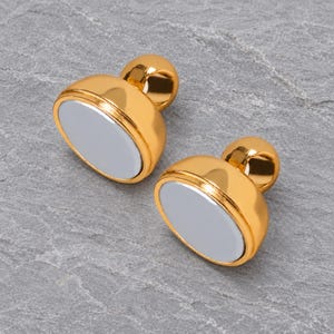 Two matching gold-tone magnetic clasp halves on natural grey stone, showing their circular contact faces, domed bodies and complete attachment eyes.
