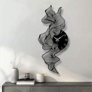 May include: Black and silver abstract wall clock. The clock has a black circular face with Roman numerals and silver hands. A flowing, wave-like design surrounds the clock, creating a modern aesthetic.