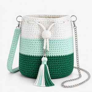 May include: A crochet bucket bag featuring a colour-blocked design in white, mint green, and dark green. The bag includes a white drawstring closure with a matching tassel, a detachable mint green crochet strap, and a silver-tone metal chain strap.