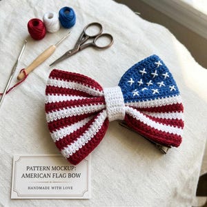 May include: Handmade crocheted bow in the style of the American flag, featuring red and white stripes and a blue section with white stars. The image includes crochet hooks, scissors, and spools of red, white, and blue yarn.