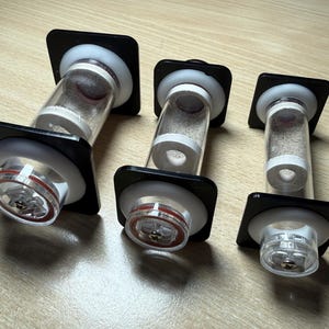 May include: Three cylindrical clear acrylic tubes with white internal rings and black square end caps. Each tube features a central clear chamber with a small white ring inside, secured by a metal screw at the base and a red circular gasket seal.