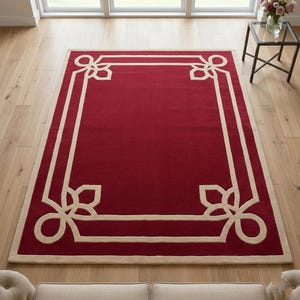 Könnte beinhalten: Ein rechteckiger roter Teppich mit cremefarbenem Rand und dekorativen Eckmustern. Der Teppich liegt auf einem hellen Holzboden. Das Design hat einen cremefarbenen Rand mit dekorativen Mustern.