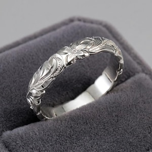 Könnte beinhalten: Ein polierter silberfarbener Metallring mit einem komplizierten gravierten Blumenmuster, detaillierten Blütenblättern und geschwungenen Blattmotiven, die sich um die gesamte Außenfläche des Bandes ziehen und eine texturierte Oberfläche bilden.