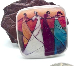 Puede incluir: Azulejo de cerámica cuadrado con una imagen colorida de cuatro mujeres tomadas de la mano y bailando. Las mujeres visten vestidos coloridos y el fondo es una puesta de sol.