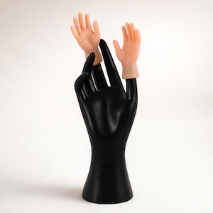 May include: A black hand-shaped display stand with two small, realistic-looking hand props. The props are flesh-toned and appear to be miniature replicas of human hands. The stand is smooth and glossy, set against a white background.