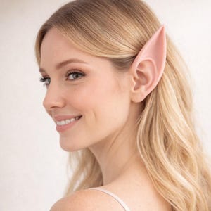 May include: A person with long blonde hair wearing a pair of pink elf ears. The ears are pointed and have a realistic design. The person is smiling and looking to the side.