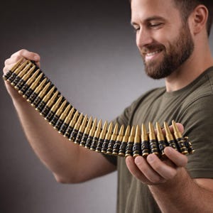 May include: A bandolier of gold-colored bullets with black detailing. The bullets are held in a row, with each bullet pointing in the same direction. The bandolier is held by a person wearing a green shirt.