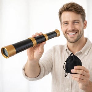 May include: A black and gold telescope with a black drawstring bag. The telescope has gold accents on the ends and in the middle. The person in the image is holding the telescope and bag.