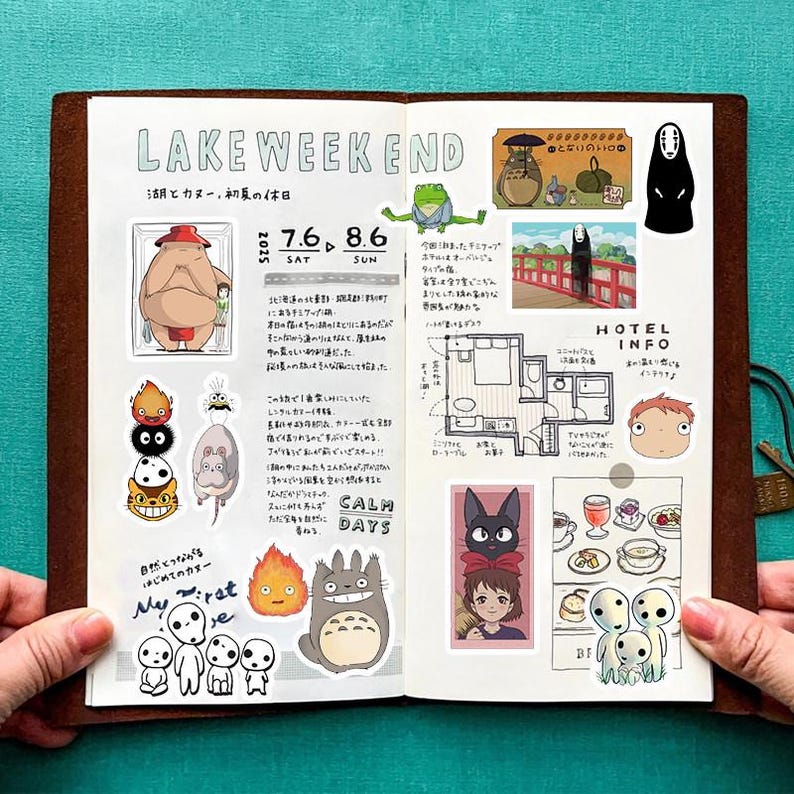 May include: A brown leather journal open to a spread with stickers of animated characters. The left page has the text "LAKE WEEKEND" and "CALM DAYS". Stickers include a large character, a mouse, and a Totoro. The right page has a map and a character.