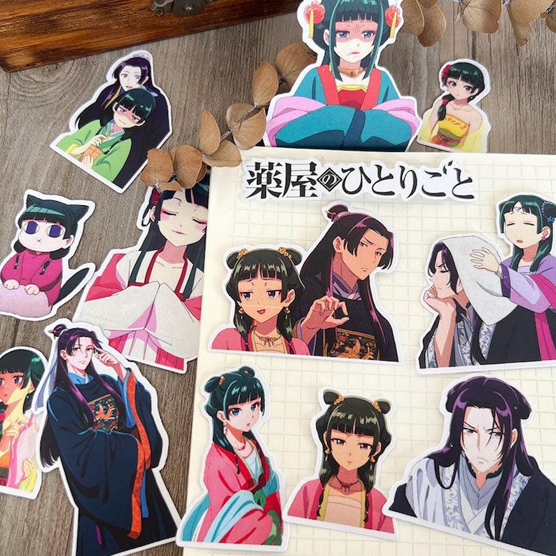May include: A selection of anime-style stickers depicting characters in traditional Asian clothing. The stickers display characters with detailed facial features and vibrant outfits. The text "薬屋のひとりごと" is present on a notepad.