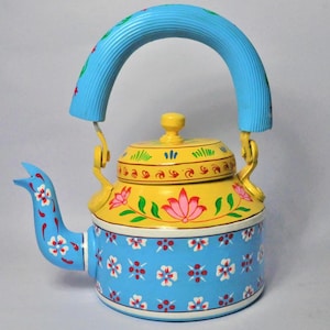 May include: A hand-painted teapot with a blue handle and spout. The body is yellow and blue, decorated with floral patterns in red, white, and green. The lid is yellow with a small knob.