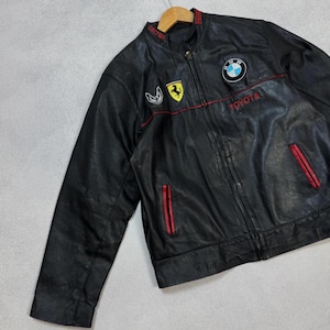 Peut inclure: Veste en cuir noir avec des détails rouges et des logos brodés. Comprend un emblème Ferrari, le logo BMW et le mot "TOYOTA" en rouge. La veste a une fermeture éclair et un col montant.