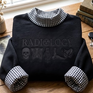 May include: A black long-sleeve sweatshirt featuring a mock neck collar with a black and white gingham pattern. The chest displays the word RADIOLOGY in embossed lettering, accompanied by embroidered anatomical illustrations of a skull, rib cage, hand, foot, and pelvis.