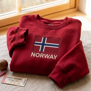 以下が含まれることがあります： 胸元にノルウェーの国旗の刺繍と白い大文字でNORWAYの文字があしらわれた、ダークレッドのクルーネックのスウェットシャツ。長袖で袖口と襟元はリブ編みになっており、すっきりとした構造的なデザインが特徴です。
