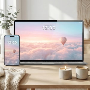 Może przedstawiać: Laptop i smartfon wyświetlają tapetę z balonem na gorące powietrze nad chmurami. Na obu ekranach wyświetlana jest godzina 12:00. Zapalona świeca i kubek kawy stoją na drewnianym stole.