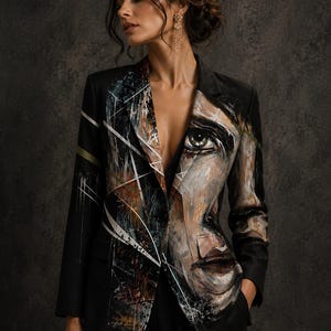 May include: A black blazer featuring a hand-painted portrait of a face on the left side and abstract geometric white lines with textured paint strokes on the right lapel. The jacket has long sleeves, a notched collar, and a single button closure.
