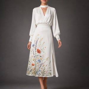 May include: A white midi dress featuring a mock neck with a cutout, long sleeves with buttoned cuffs, and a wrap-style bodice. The skirt displays a colorful botanical print of wildflowers, including red poppies and blue cornflowers, with a side slit.