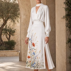 May include: A white midi dress with long sleeves, a high neck with a cutout, and a side slit. The skirt features a colorful floral print of wildflowers including red poppies and blue cornflowers. The cuffs also display small floral embroidery.