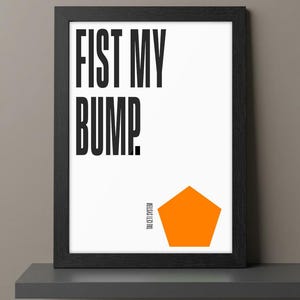 May include: Black framed art print with the text "FIST MY BUMP" in bold black letters on a white background. An orange pentagon shape is at the bottom right. The text "TAU CETI SYSTEM" is printed vertically on the right side.