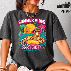 Peut inclure: T-shirt gris foncé avec un graphisme coloré. Le graphisme représente un léopard portant des lunettes de soleil et un chapeau, flottant sur un anneau gonflable jaune. Le texte dit "Summer Vibes Good Times & Tan Lines."
