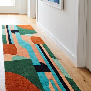 Puede incluir: Una colorida alfombra geométrica para pasillo con un diseño moderno. La alfombra presenta una combinación de formas verdes, naranjas, turquesas y negras. La alfombra es rectangular y está colocada en un pasillo.