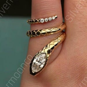 May include: A gold snake ring with a textured design. The snake's head has a marquise-cut diamond, and the ring coils around the finger. The ring has a small band with three small diamonds. The text "Silvermoonco" is visible.