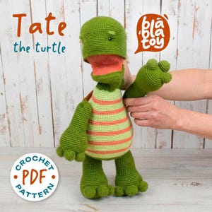 May include: A handmade green crochet turtle named "Tate" with orange and green striped shirt. The turtle has a large head, open mouth, and outstretched arm. The image includes the text "bla toy" and "CROCHET PDF PATTERN".