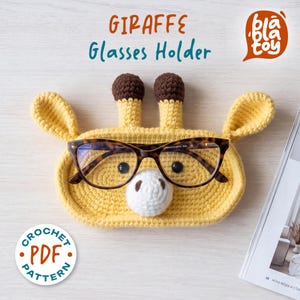 May include: A yellow crocheted giraffe glasses holder with brown accents, holding a pair of eyeglasses. The holder has a white nose and black eyes. The text "GIRAFFE Glasses Holder" is at the top. A "Crochet PDF Pattern" logo is in the bottom left.