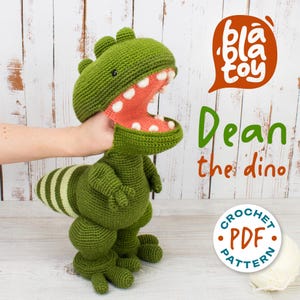 Op de afbeelding: Een groen gehaakt dinosaurus speelgoed met een open mond die witte tanden en een roze binnenkant laat zien. De dinosaurus heeft een gestreepte staart en is gelabeld "Dean the dino" met de tekst "Crochet PDF Pattern".