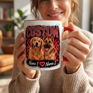 Puede incluir: Taza de cerámica blanca con interior y asa rojos, con un diseño personalizado. El diseño incluye la palabra "CUSTOM" en rojo, dos retratos de perros y espacio para dos nombres. La taza está sujeta por una persona.