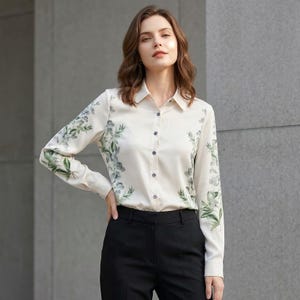 Puede incluir: Camisa crema con botones, mangas largas y un estampado floral en tonos verdes y grises. La camisa se combina con pantalones negros. La camisa tiene un cuello clásico y puños abotonados.